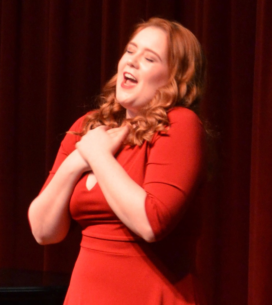 A woman in red dress singing on stage.